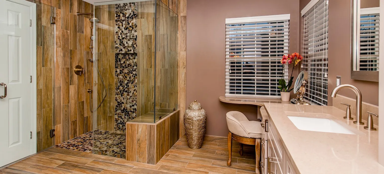 Modern Brookville, MD bathroom remodel with wood-look tile walls, pebble accent walk-in shower, and tan vanity.